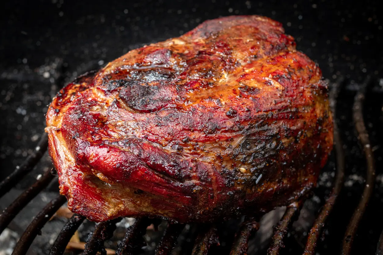 Pork shoulder piece of meat grilling on the smoker. 